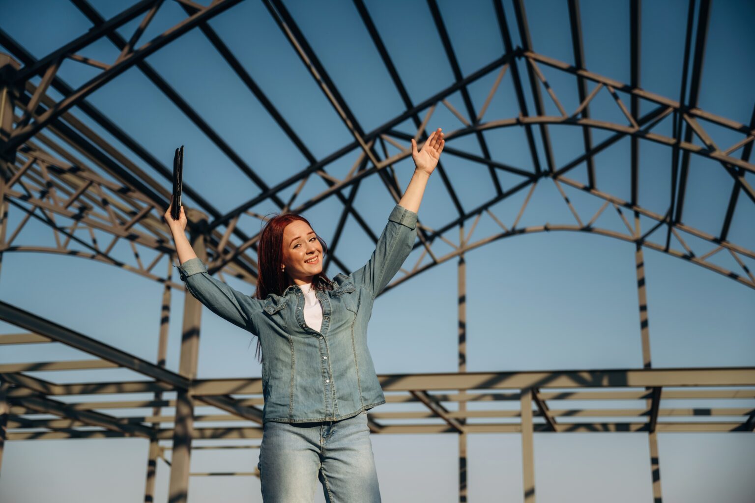 Young redhead woman is standing near unfinished building, construction.