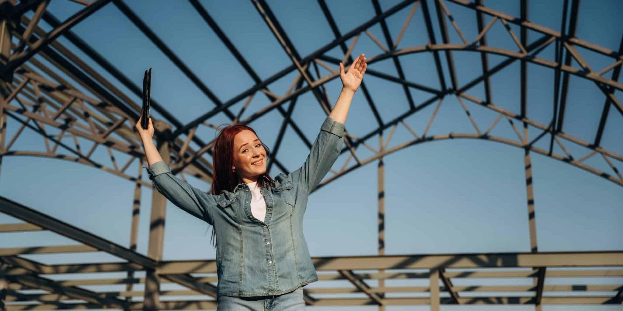 Young redhead woman is standing near unfinished building, construction.